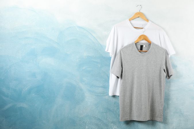 Hangers with blank and gray t-shirts on blue background, copy space
