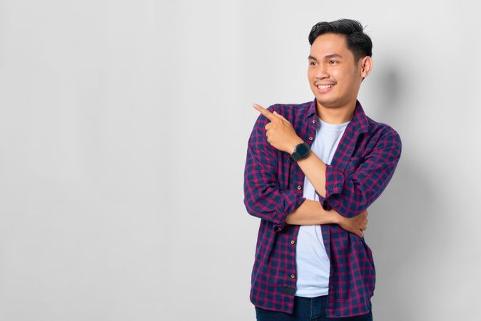 Smiling Asian male in grey studio with pointing thumb to the side