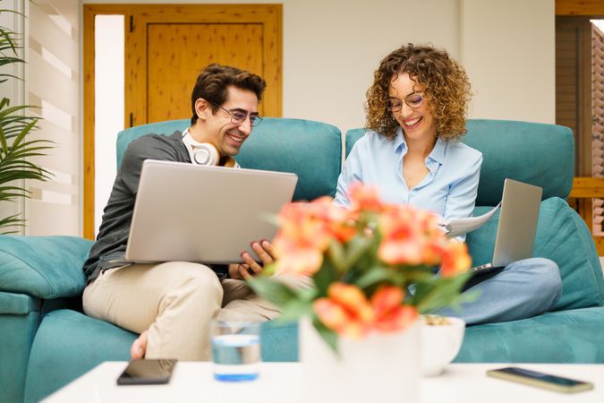 Couple laughing as they work from together in their living room