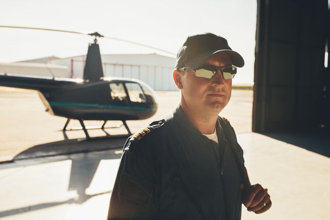 Helicopter pilot in cap and sunglasses inside hangar