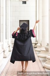 Woman walking in hallway wearing mortarboard and academic gown 56yBY0