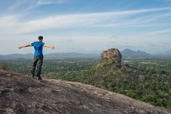 Tourist against solitary rock in middle of green forested plain under clear sky in summer