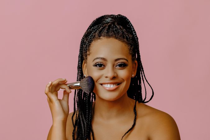 Happy woman applying make up with brush to her cheek