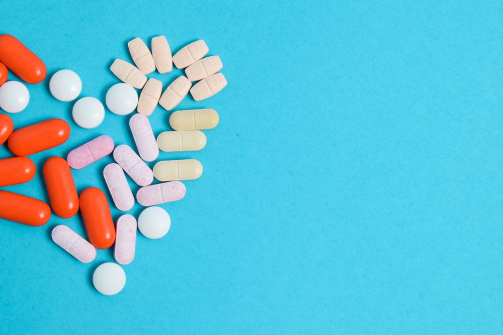 Mix of pIlls in heart shape on blue background with copy space