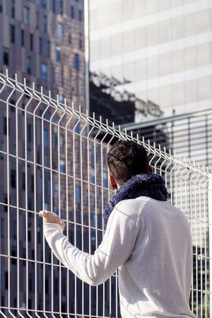 Man leaning on a metallic fence while looking up to the business buildings, vertical