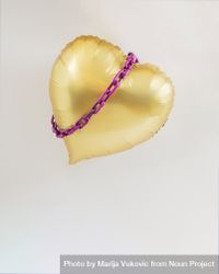 Gold heart balloon in the air with violet purple chains around it 0K6JYb