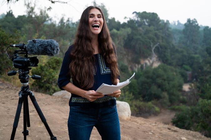 Woman laughing with script in hand standing next to a camera