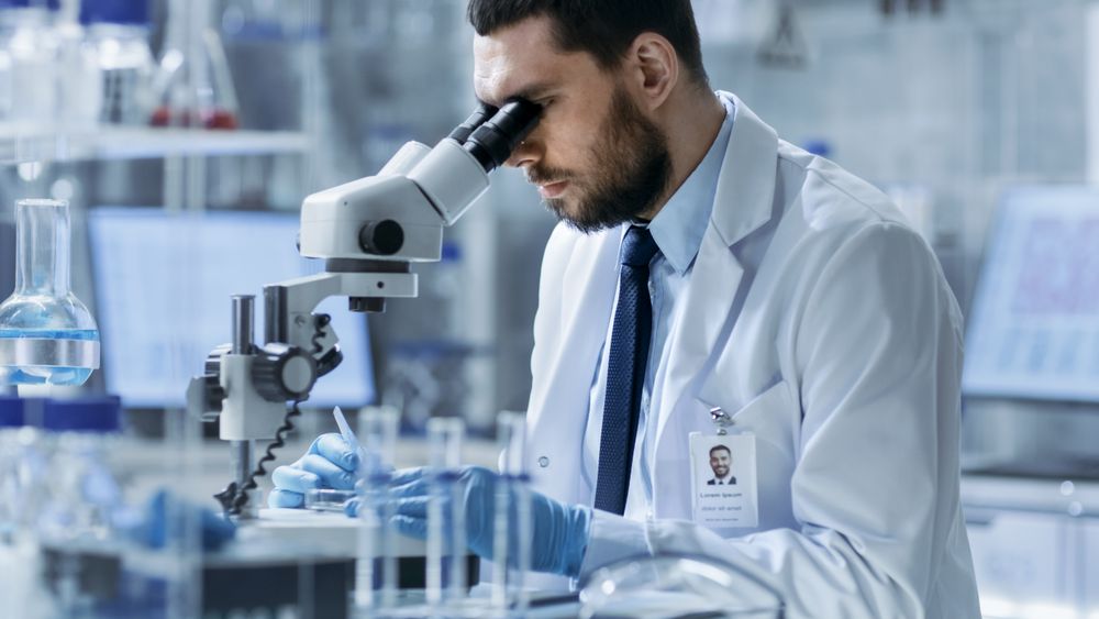 Research Scientist Adjusts Specimen in a Petri Dish and Looks on it Into Microscope.