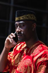Black male in traditional clothes talking on cellphone in street