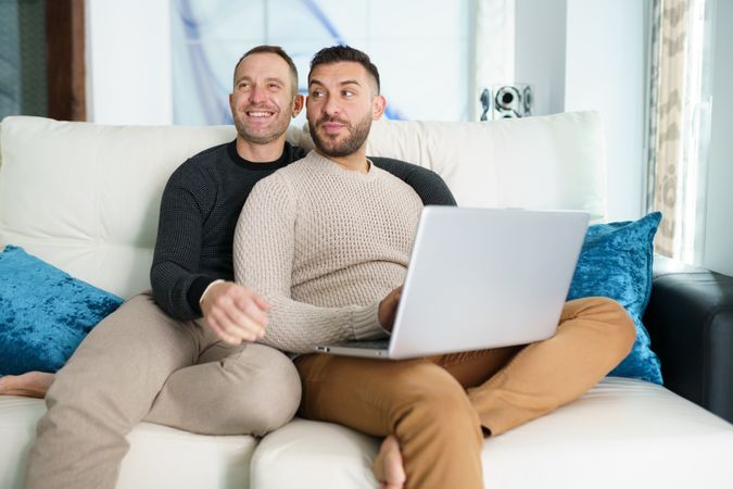 Male couple relaxing on couch with laptop