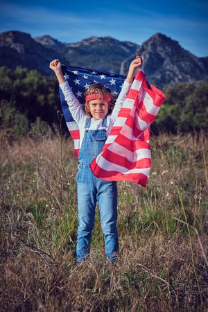 Proud preteen boy raising hands with American national flag