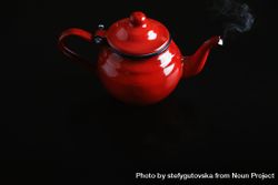 Shiny red tea pot on dark table with steam rising from spout 5XGqP0