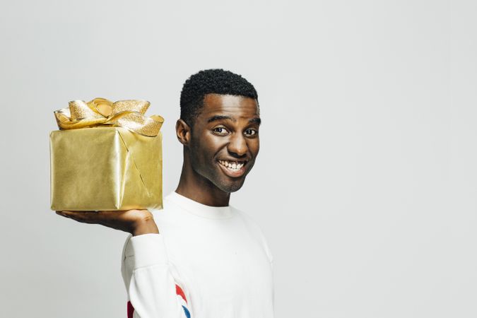 Smiling Black man holding a present wrapped in gold on his shoulder