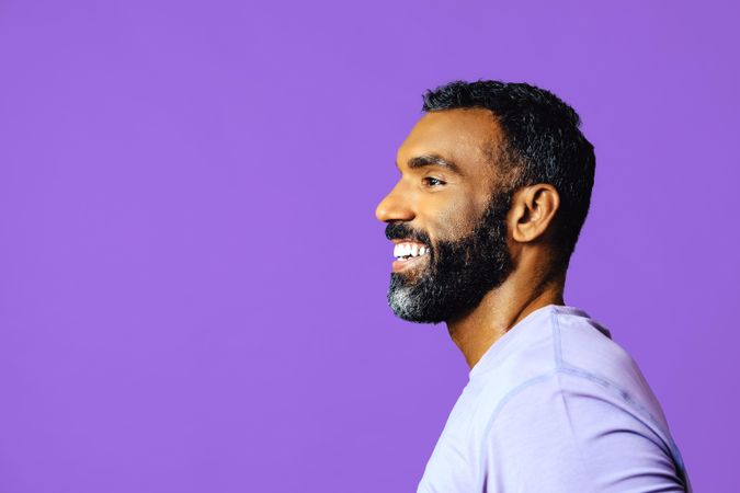 Side view of smiling male in purple t-shirt looking to the side, copy space
