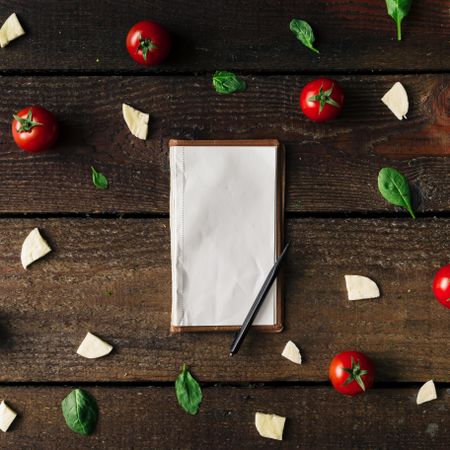 Basil, tomatoes, and cheese on wooden background with notepad