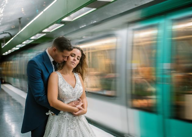 Satisfied bride couple in wedding suits standing in an embrace at metro
