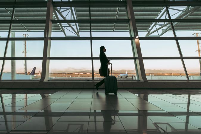 Silhouette of female flight passenger with luggage walking at airport terminal