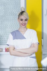 Smiling blonde dentist with her arms folded at work bEdvn4