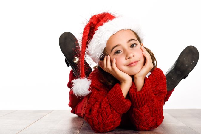Child in santa outfit lying on stomach on ground resting her head on her hands