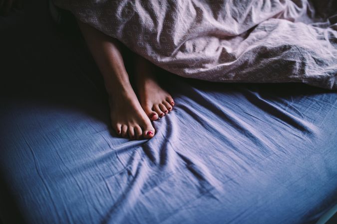 Woman’s feet peaking out from the blankets while lying in bed