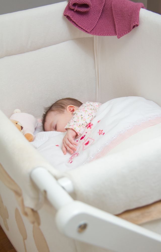 Baby girl sleeping in a cot with pacifier and toy