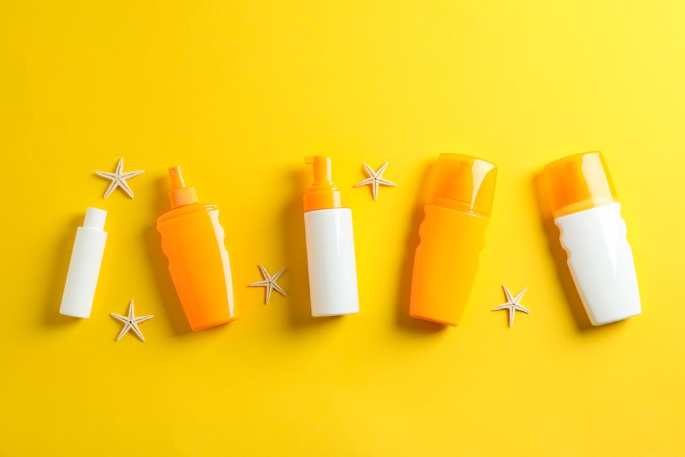 Flat lay composition with sunscreen sprays and starfishes on color background, space for text. Summer vacation backdrop