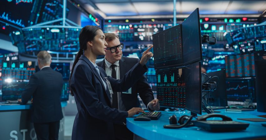 Asian Female and Male Stock Exchange Agents Using Computer, Discussing Investment Strategy for an International Business Client, Working in an Office Building Surrounded by Computer Screens