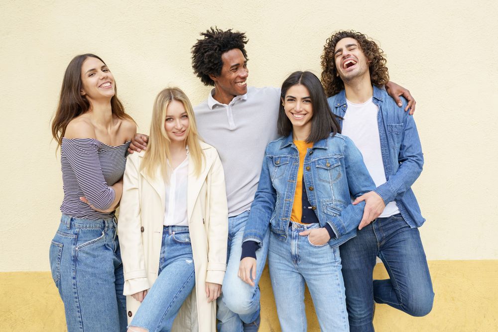Smiling friends posing for photo leaning against a yellow wall
