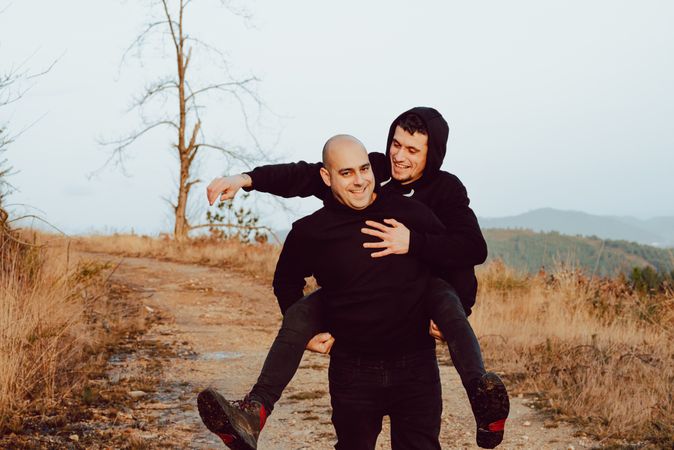 Smiling man holding on back cheerful guy on road on hill