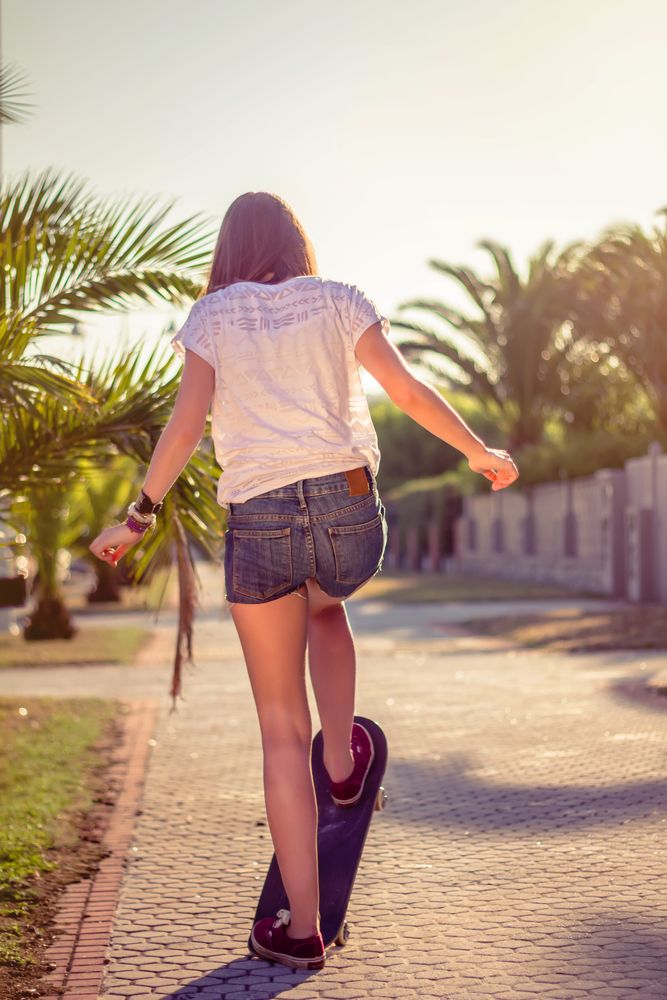 Back view of girl riding in a skateboard outdoors on summer