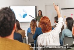Businesswoman with red hair raising hand to ask question during a SWOT analysis presentation in large office room bGRNme