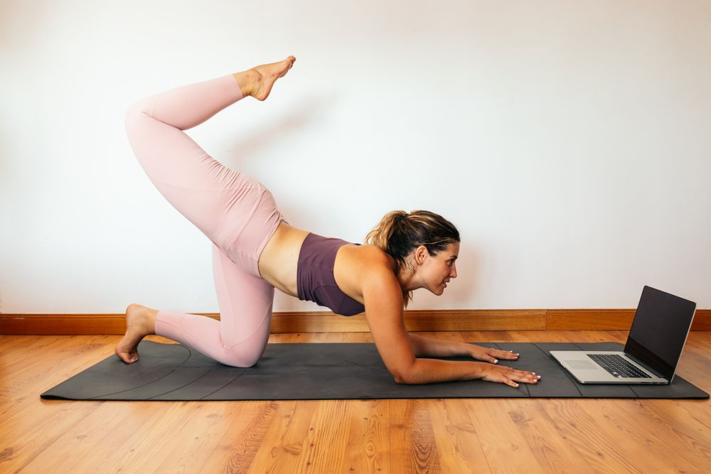 Woman in sportswear doing yoga with laptop at home