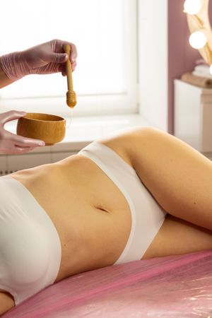 Spa practitioner dripping honey on stomach during skin treatment.