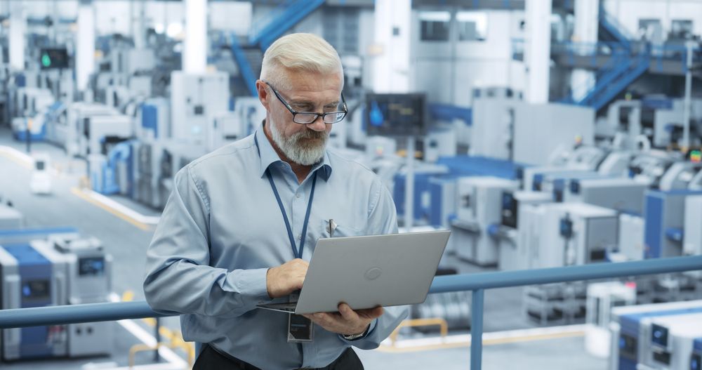 Mature Engineer Monitoring and Analyzing Conditions at an Automated Modern Electronics Factory with Mobility Robots Working with the Help of Artificial Intelligence Software
