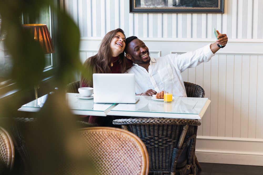 Cheerful multiethnic couple using laptop at home while taking a selfie