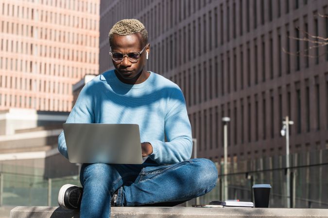 Stylish young Black man working remotely on laptop in city park