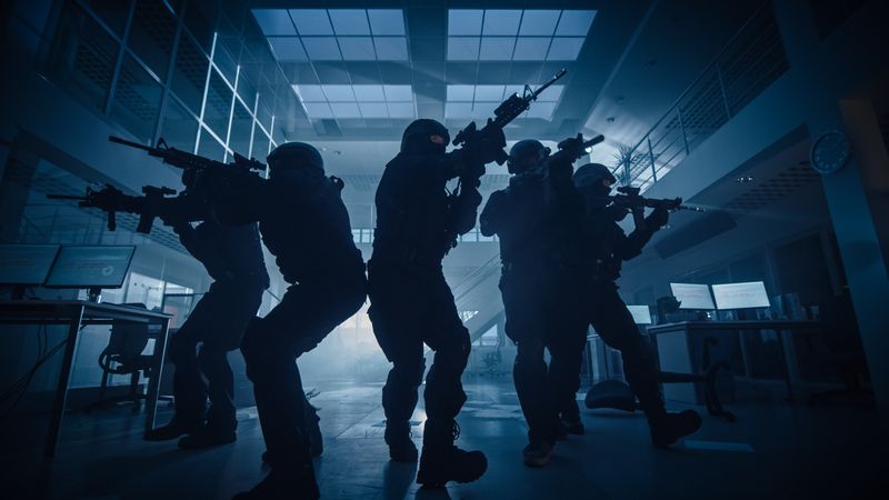 Masked Team of Armed SWAT Police Officers Move in a Hall of a Dark Seized Office Building with Desks and Computers.