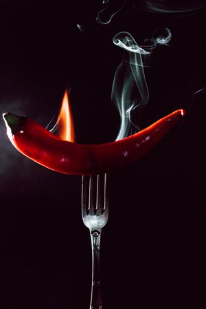 red chili pepper on fire in fork on a dark background
