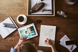 Top view of woman sketching with coffee, camera, and tablet on table