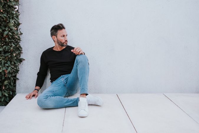 Adult stylish man sitting near grey wall