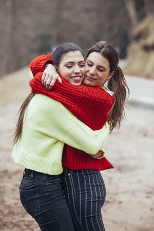 Smiling women in sweaters hugging in park