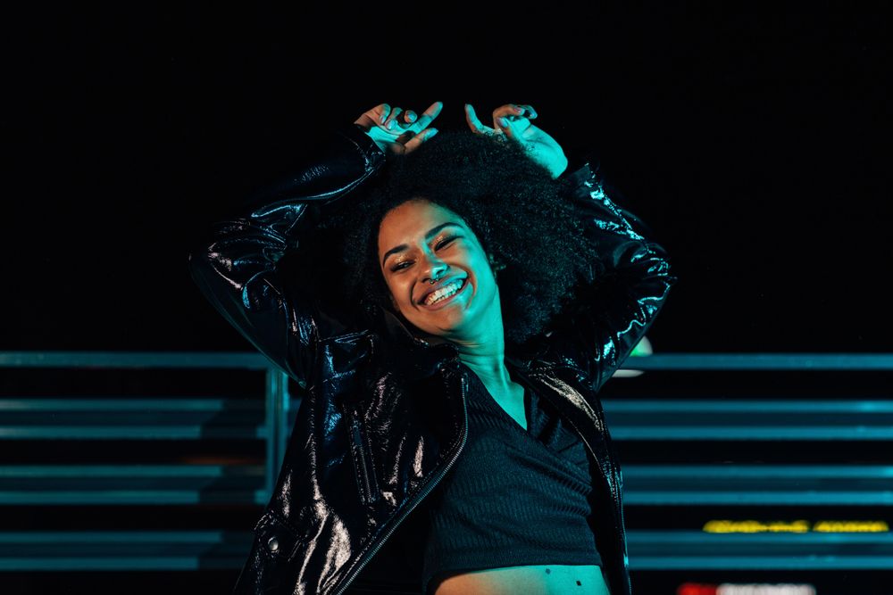 Happy Black woman on a rooftop in blue green light with her arms up
