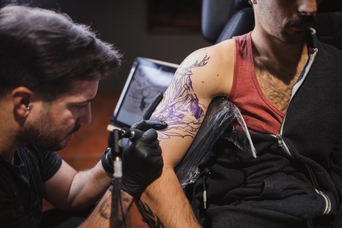 Master doing tattoo on forearm of male customer