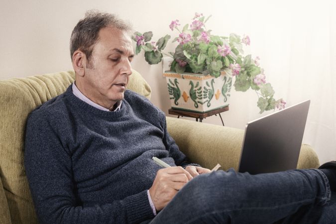 Mature man studying or working from home on his sofa.