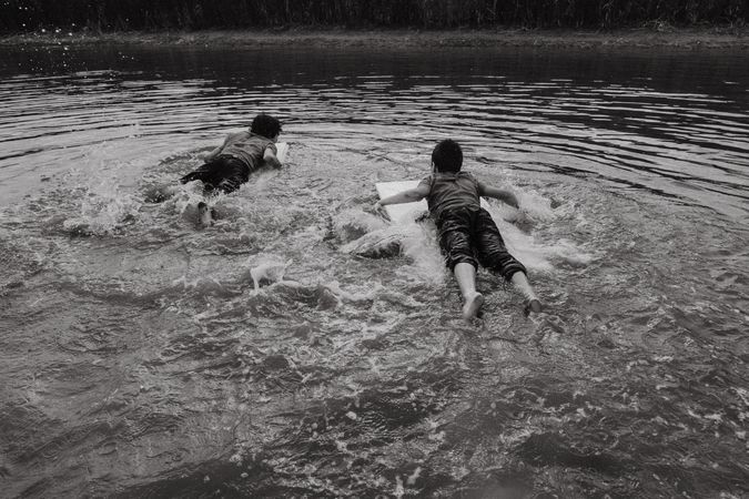 Happy boys swimming with board over water
