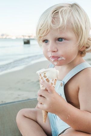 Charming boy eating ice cream on beach