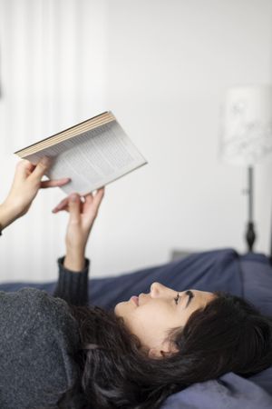 Young woman laying in bed reading a book