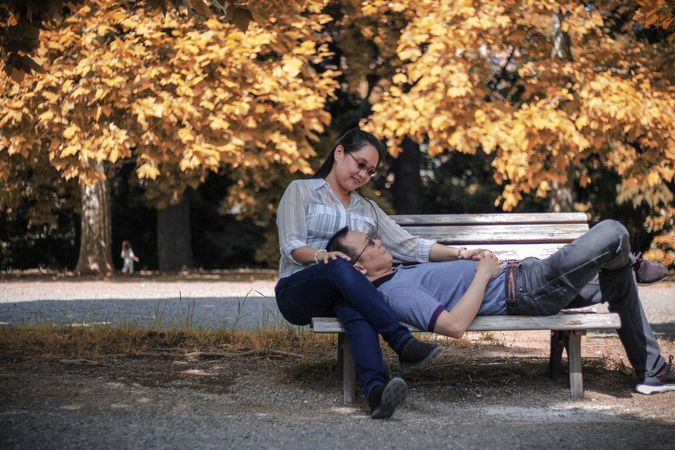 Man leaning his head on woman's lap sitting on brown wooden bench