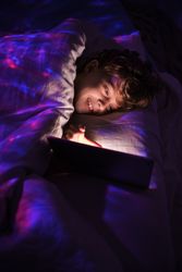 Positive boy browsing tablet in dark bedroom
