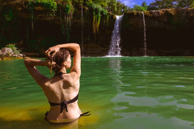 Anonymous woman touching hair and looking at waterfall